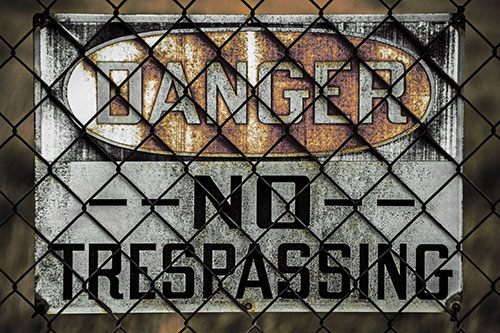Dirty Danger No Trespassing Sign Behind Chain Link Fence (Orange Tint)
