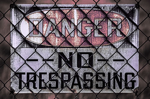 Dirty Danger No Trespassing Sign Behind Chain Link Fence (Pink Tint)