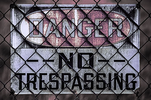 Dirty Danger No Trespassing Sign Behind Chain Link Fence (Purple Tint)