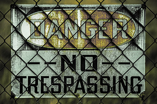 Dirty Danger No Trespassing Sign Behind Chain Link Fence (Yellow Tint)